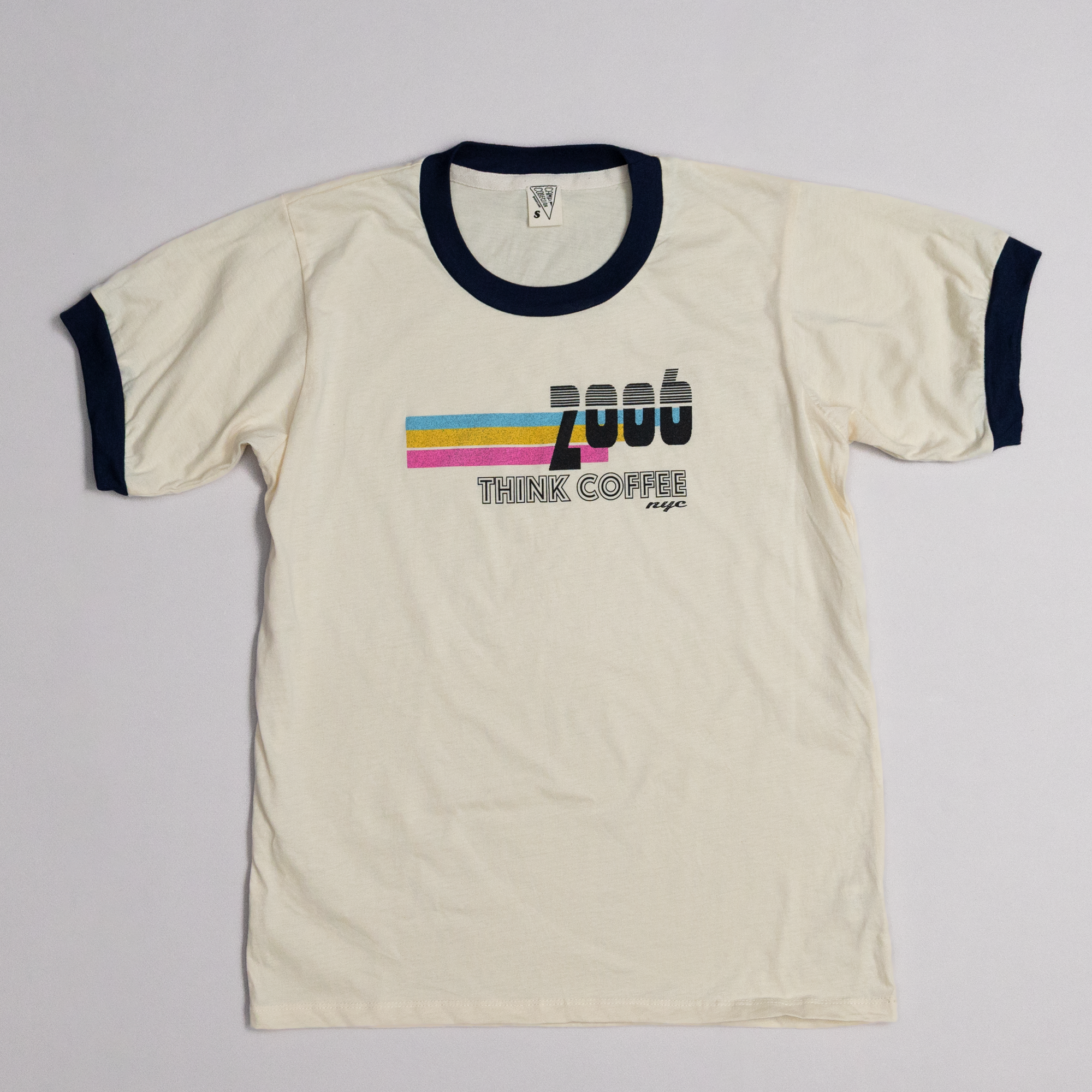 Beige t-shirt with colorful text and stripes on a light gray background