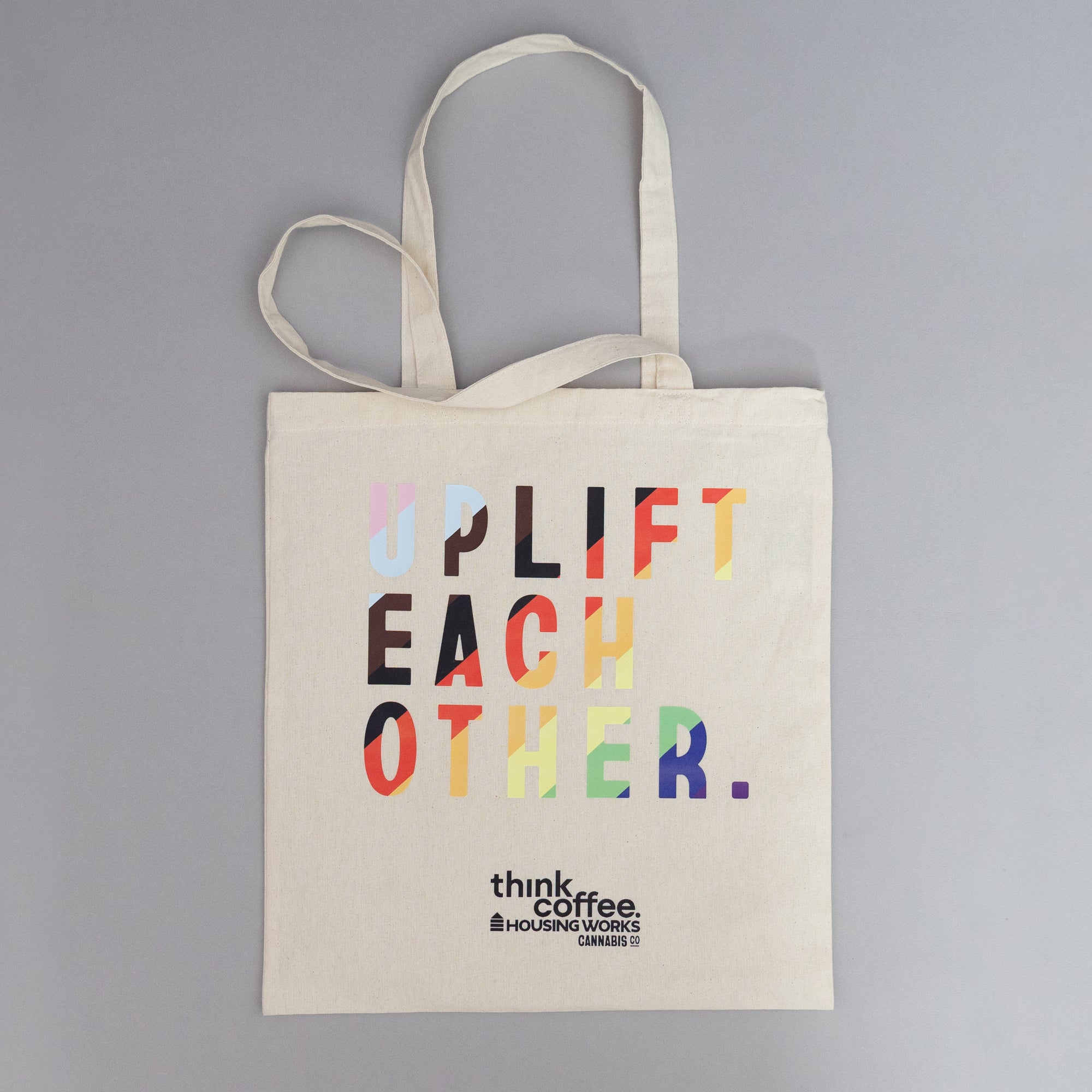 Beige tote bag with colorful text 'Uplift Each Other' ThinkCoffee" merch